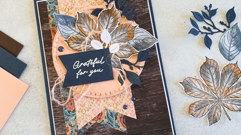 Handmade cared using Artistic Leaves stamps from Stampin' Up! The card is in shades of espresso, petal pink and secret sea dark blue. The background is patterned paper with a soft apricot pink circle with stitching in the same colour. The leaves are layered on top of the circle and the white embossed sentiment says Grateful to you.