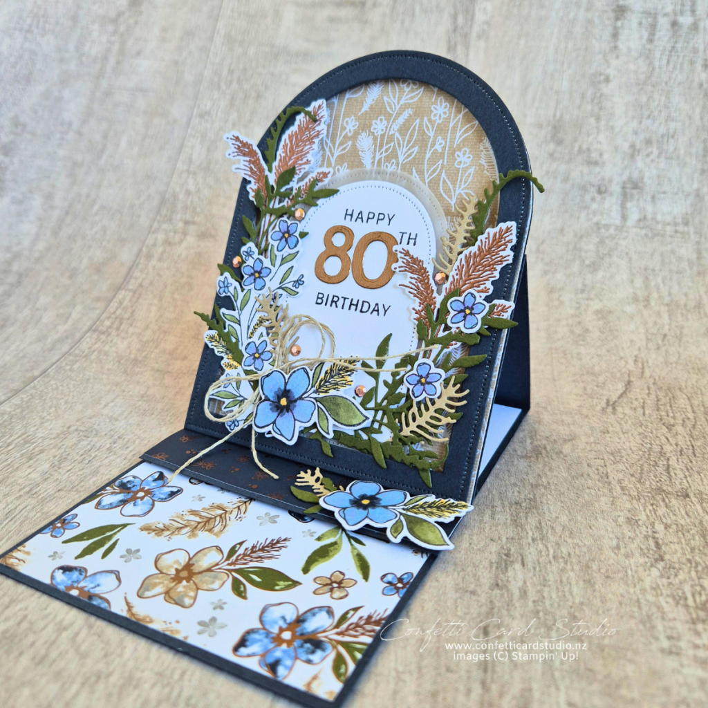 Delicate Whispers Arched Easel Card featuring blue floral layers, vellum arch, bronze accents and an 80th birthday sentiment on a raised easel base
