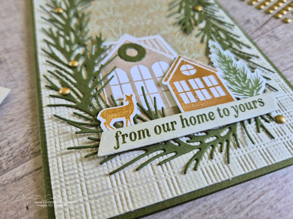 Neutral Noel Christmas card featuring die-cut green pine branches, two little houses, a deer and gold embellishments on a textured beige background.