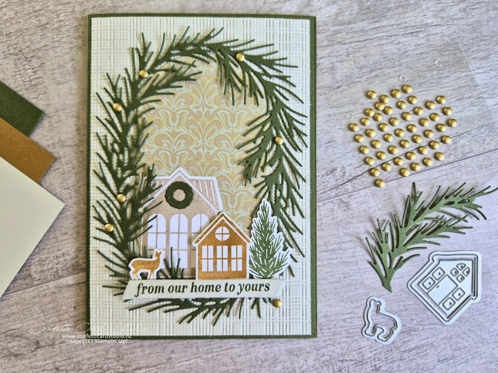 Neutral Noel Christmas card featuring die-cut green pine branches, two little houses, a deer and gold embellishments on a textured beige background.