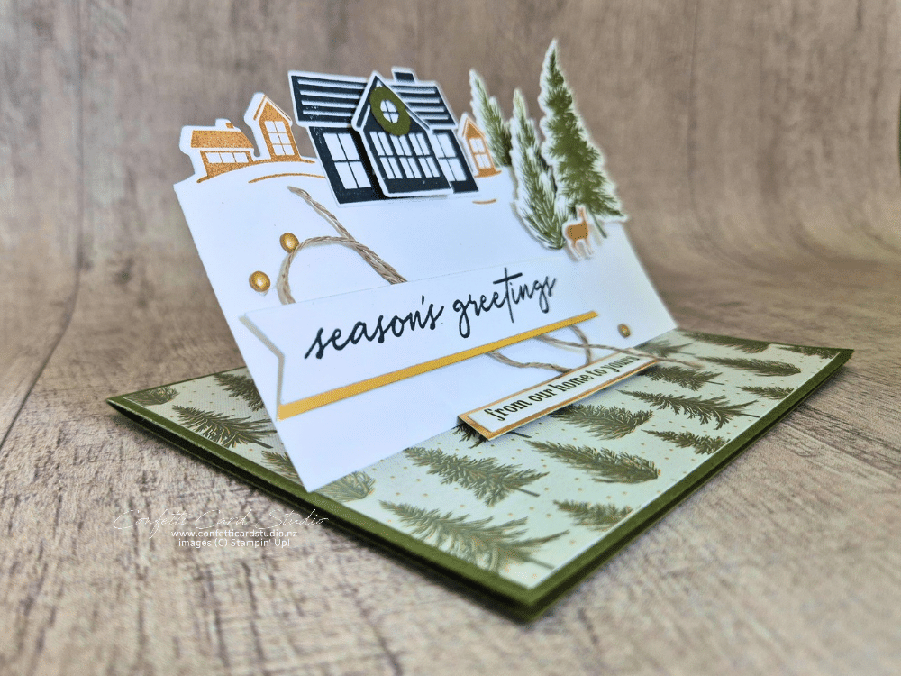 Stampin’ Up! Welcome Noel easel Christmas card with a village scene, evergreen trees, woodland deer, gold accents and a Season’s Greetings banner.