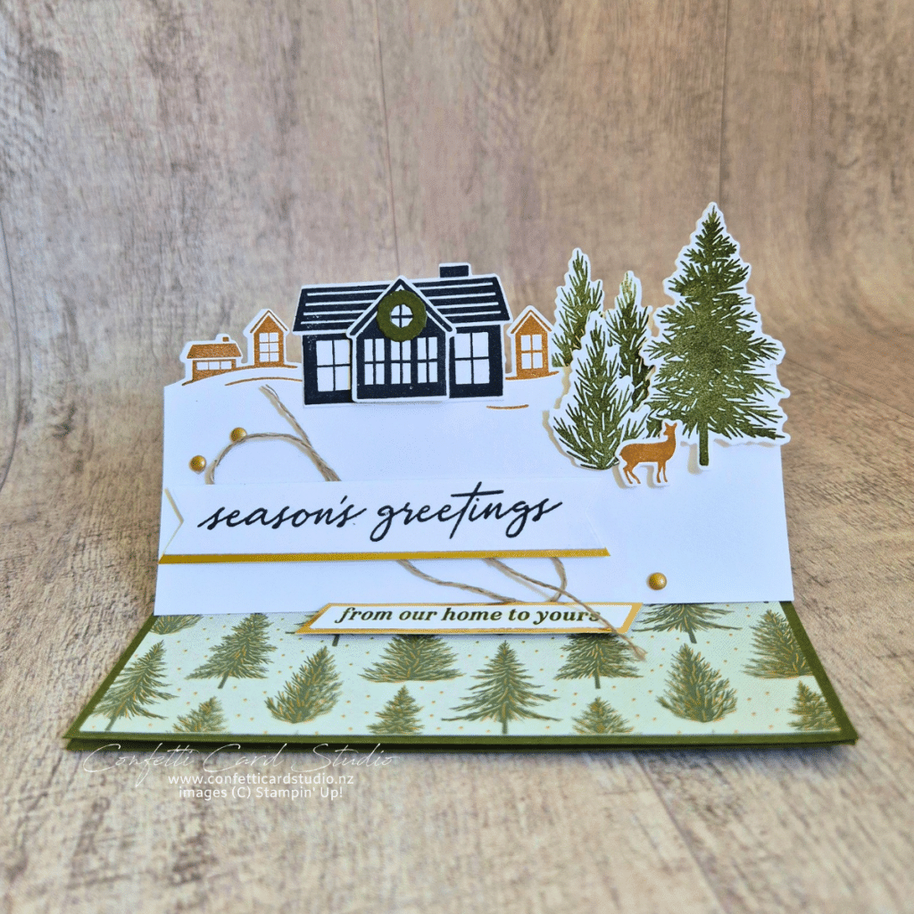 Stampin’ Up! Welcome Noel easel Christmas card with a village scene, evergreen trees, woodland deer, gold accents and a Season’s Greetings banner.